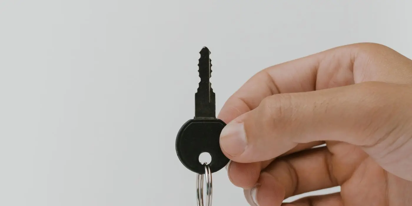 A hand holding a single key against a plain background